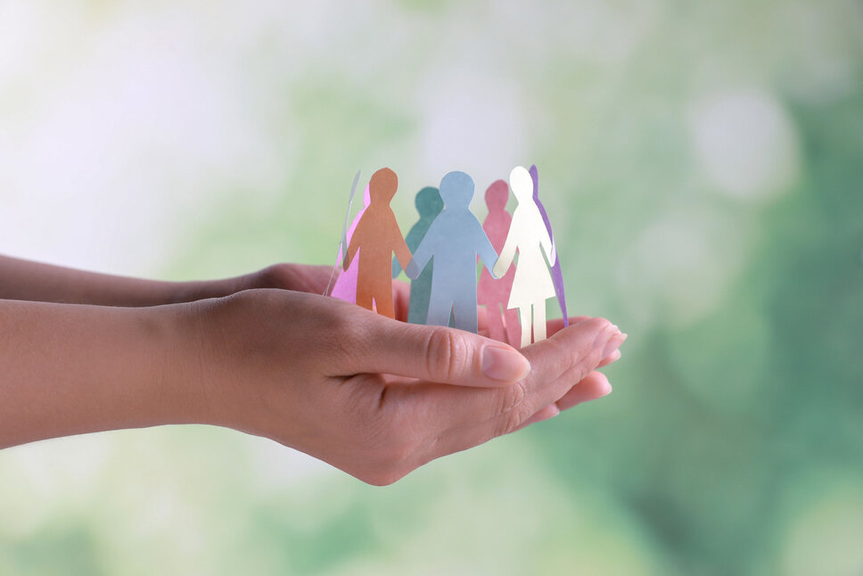 Close-up of hands holding human paper figures, set against a blurred background. This image illustrates the concept of diversity and inclusion. In the business ethics of weba Werkzeugbau, this image symbolizes the policy for upholding human rights and compliance with labor regulations.