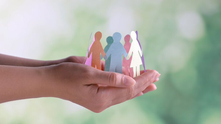 Close-up of hands holding paper cut-out human figures against a blurred background. This image illustrates the concept of diversity and inclusion. In the business ethics of weba Werkzeugbau, this image symbolizes the policy of respecting human rights and compliance with labor regulations.