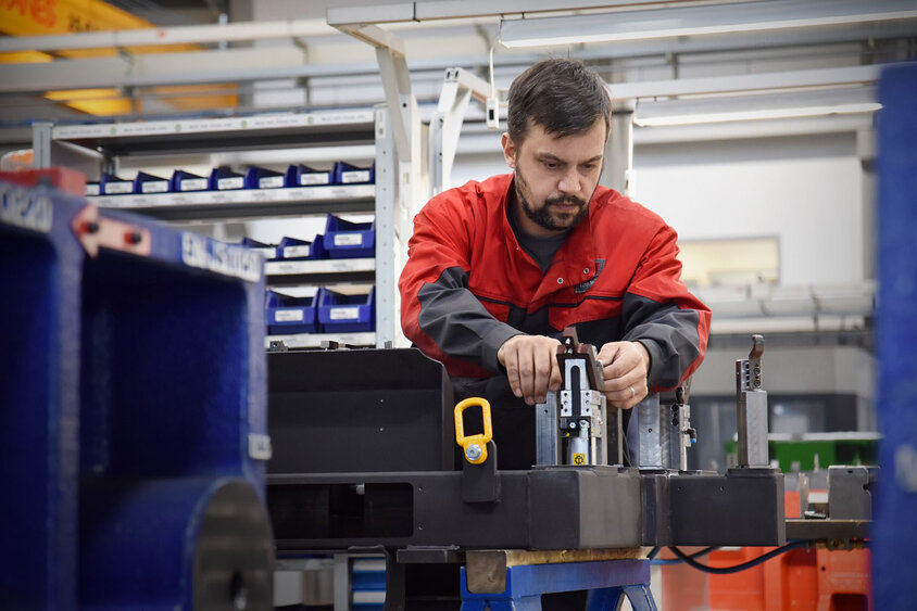 The picture shows a toolmaking technician from weba concentrating on assembling a test part gauge in a production environment. The scene is surrounded by tools, machines and other work utensils. The technician works precisely and carefully to ensure that the gauge is assembled correctly. The atmosphere exudes professionalism and efficiency as the technician prepares the gauge for use in production. The picture illustrates weba's overarching expertise in forming technology.