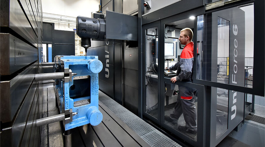 The machine operator stands concentrated in the control room of the machining center and monitors the machining process of a large casting. His gaze is fixed on the workpiece as he controls the machine and makes any necessary adjustments. The scene convey