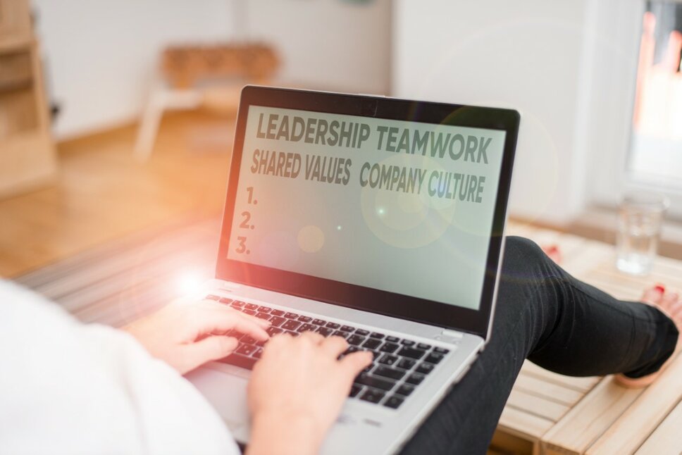 A woman sits on the floor with a laptop on her lap. The screen displays the words "Leadership, Teamwork, Shared Values, and Company Culture," while light reflects off the laptop. The image symbolizes a value-driven work culture at weba for your career in Steyr.