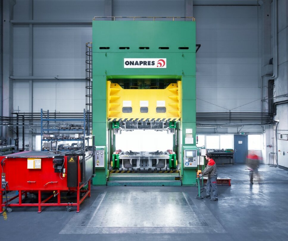 Hydraulic forming press with chamber oven, toolmaking technician at the control panel, daylight coming through the windows. Use of the forming press during a tool tryout.