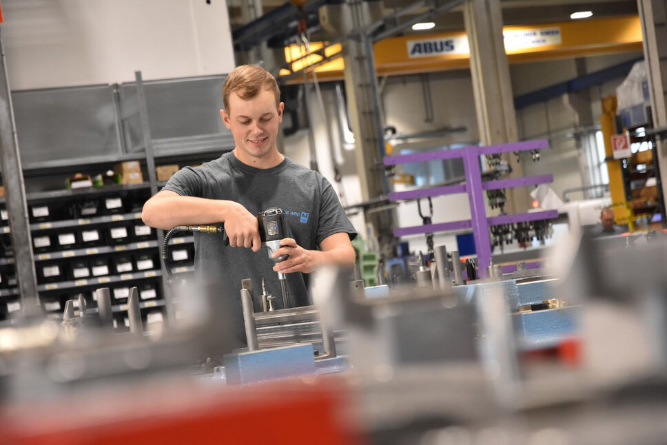 A young, smiling toolmaker in a production environment assembling a forming tool during his internship job at weba in Steyr.