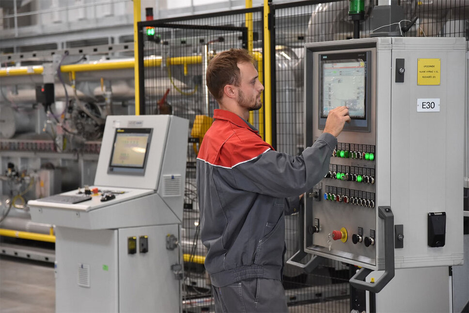 A focused machine operator at weba Werkzeugbau stands at the complex control console of the hot forming line, surrounded by bright displays and control elements.