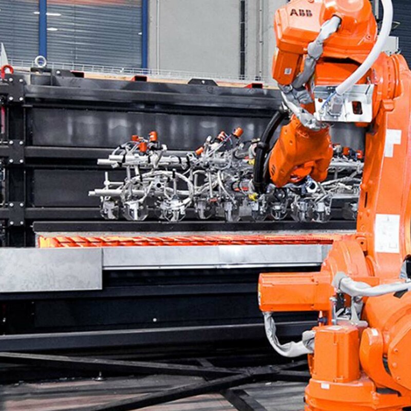 A robot arm removes four red-hot forming blanks from a chamber hot forming furnace for transfer to the forming press and component production.