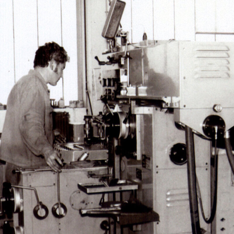 A black and white picture from the 1980s shows a machining technician operating a conventional boring machine.