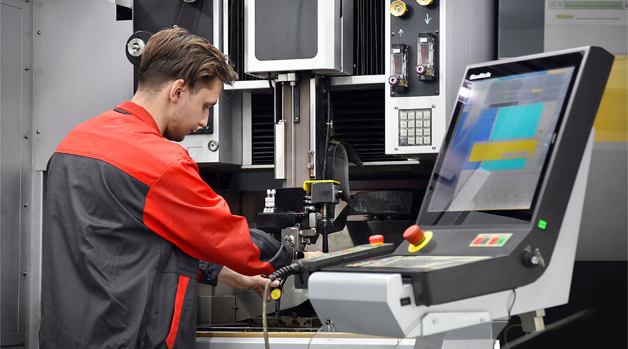 The picture shows a toolmaking technician from weba Olomouc concentrating on operating a modern EDM machine. His hands are skillfully busy controlling the machine.