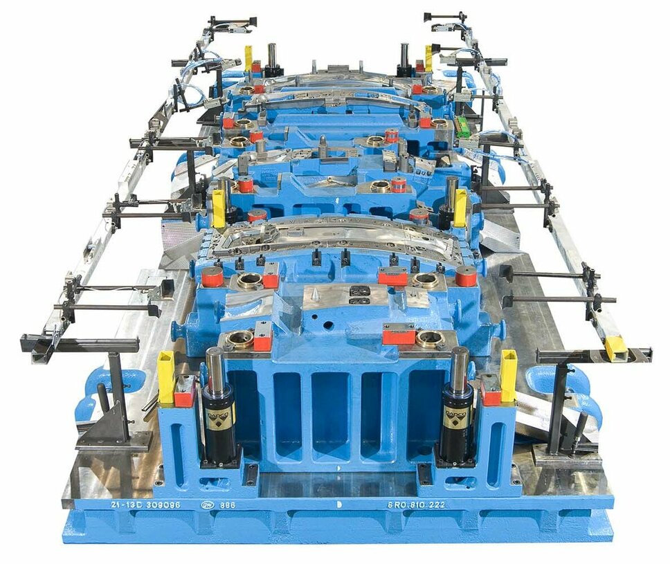  A detailed representation of a blue transfer tool for cold forming, including a transfer gripper rail for the production of B-pillars for vehicles, visualized against a neutral background. Special attention is given to the transfer gripper rail, which is precisely designed for handling and transporting B-pillars within the production line. The tool's design showcases advanced engineering, with visible details that illustrate the system's functionality and efficiency within automotive manufacturing.