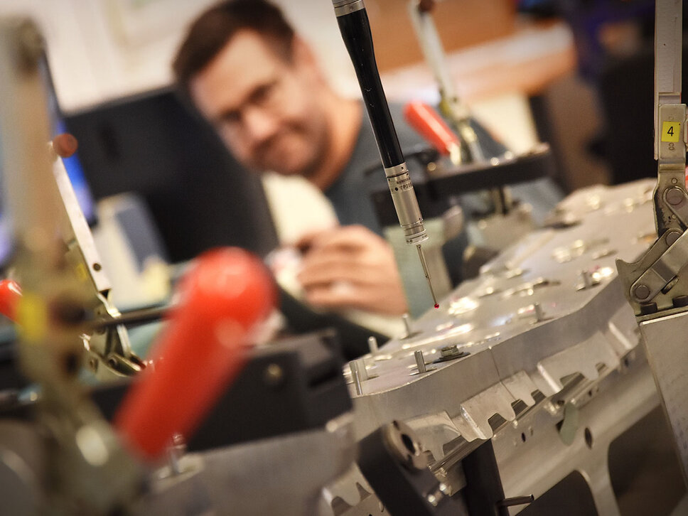 Close-up of a coordinate measuring machine with a focus on the measuring probe. In the background, the metrology technician is seen out of focus and blurred.