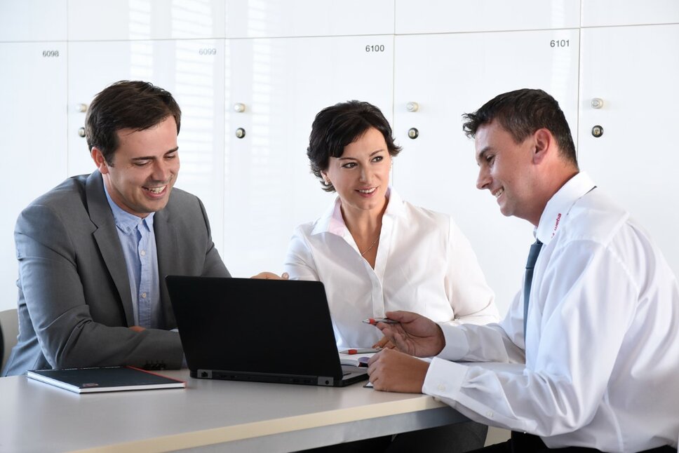 Two male employees and one female employee are in a meeting, focusing intently on the display of a shared laptop.