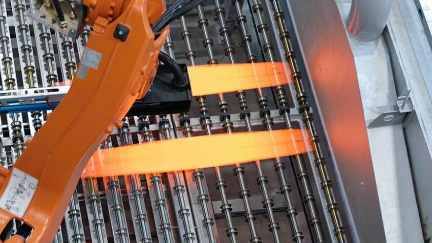 Industrieller Roboterarm in der Prozesstechnik für das Presshärten positioniert glühend heiße Metallbleche auf einer Produktionsanlage. Der Einsatz modernster Technologie optimiert den Presshärteprozess und gewährleistet eine präzise Steuerung der Umformprozesse bei weba Werkzeugbau.