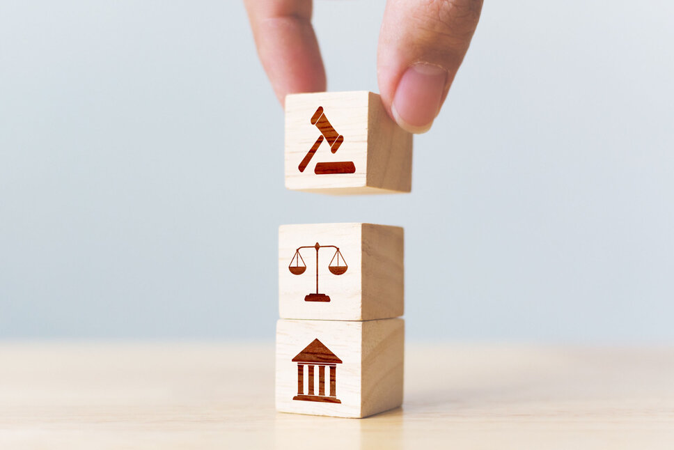 Three wooden blocks in cube form with painted icons representing the theme of justice, symbolizing stability and the rule of law. In the business ethics of weba Werkzeugbau, this image symbolizes the policy for compliance with laws and contracts.