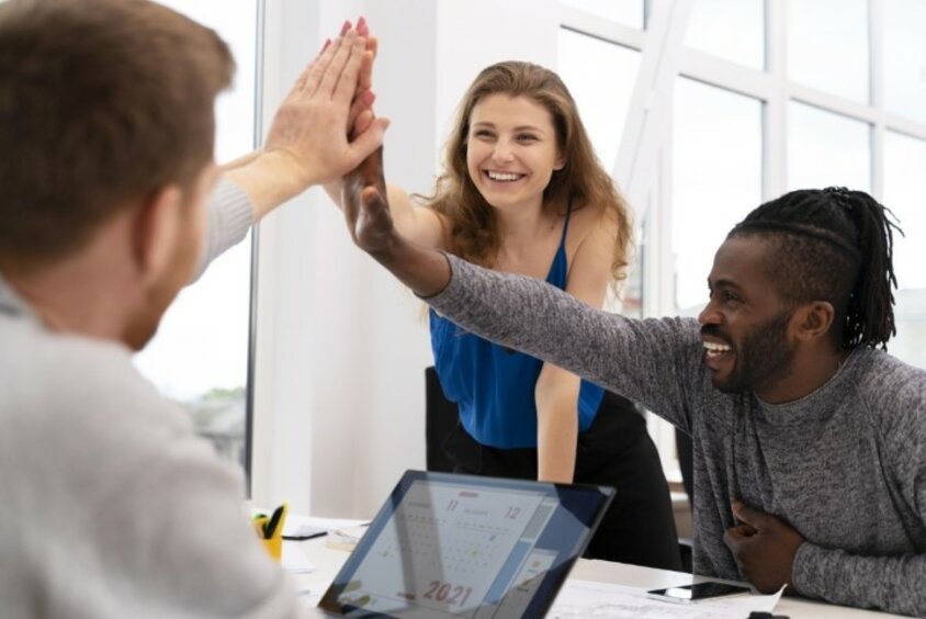 Three people are sitting at a meeting table, smiling and giving each other high-fives.