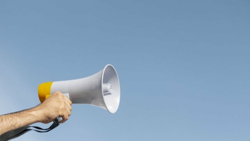 A hand holds a megaphone up against a clear blue sky without clouds, symbolizing a guide for job advertisements.