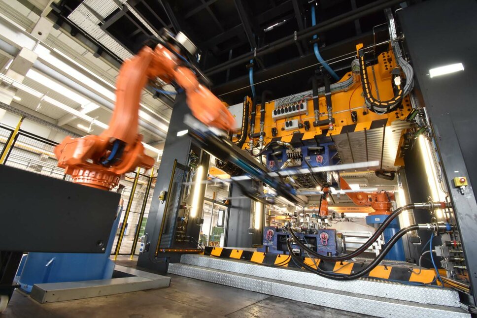 Image of a moving robotic gripper during series production, transferring manufactured components from the hot forming tool to the conveyor belt.