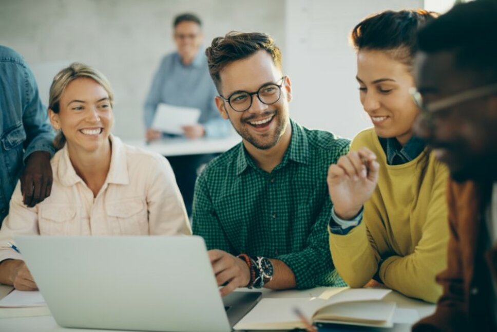 A cheerful student enjoys using a laptop with his friends in a classroom. The image symbolizes internship opportunities in Steyr for students at weba Werkzeugbau.