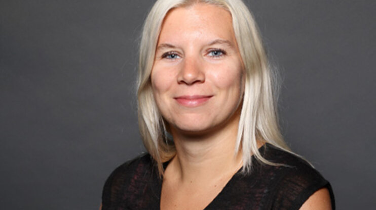 A professional portrait of Bettina Gmainer, a dedicated employee at weba Werkzeugbau, with blonde hair and a friendly smile against a neutral gray background.